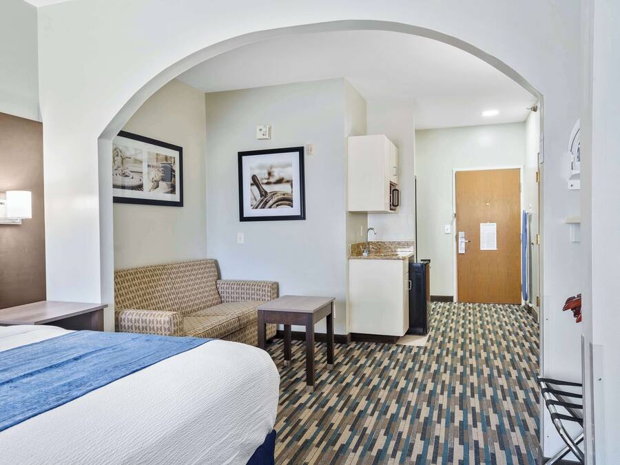 A hotel room with a bed, a sofa, a small table, a kitchenette, and an arched doorway leading to another room.