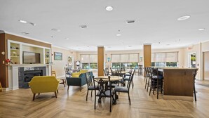 A spacious dining area with multiple tables and chairs, a fireplace, and a television. - Blue Water Inn & Suites, BW Signature Collection (Sneads Ferry)