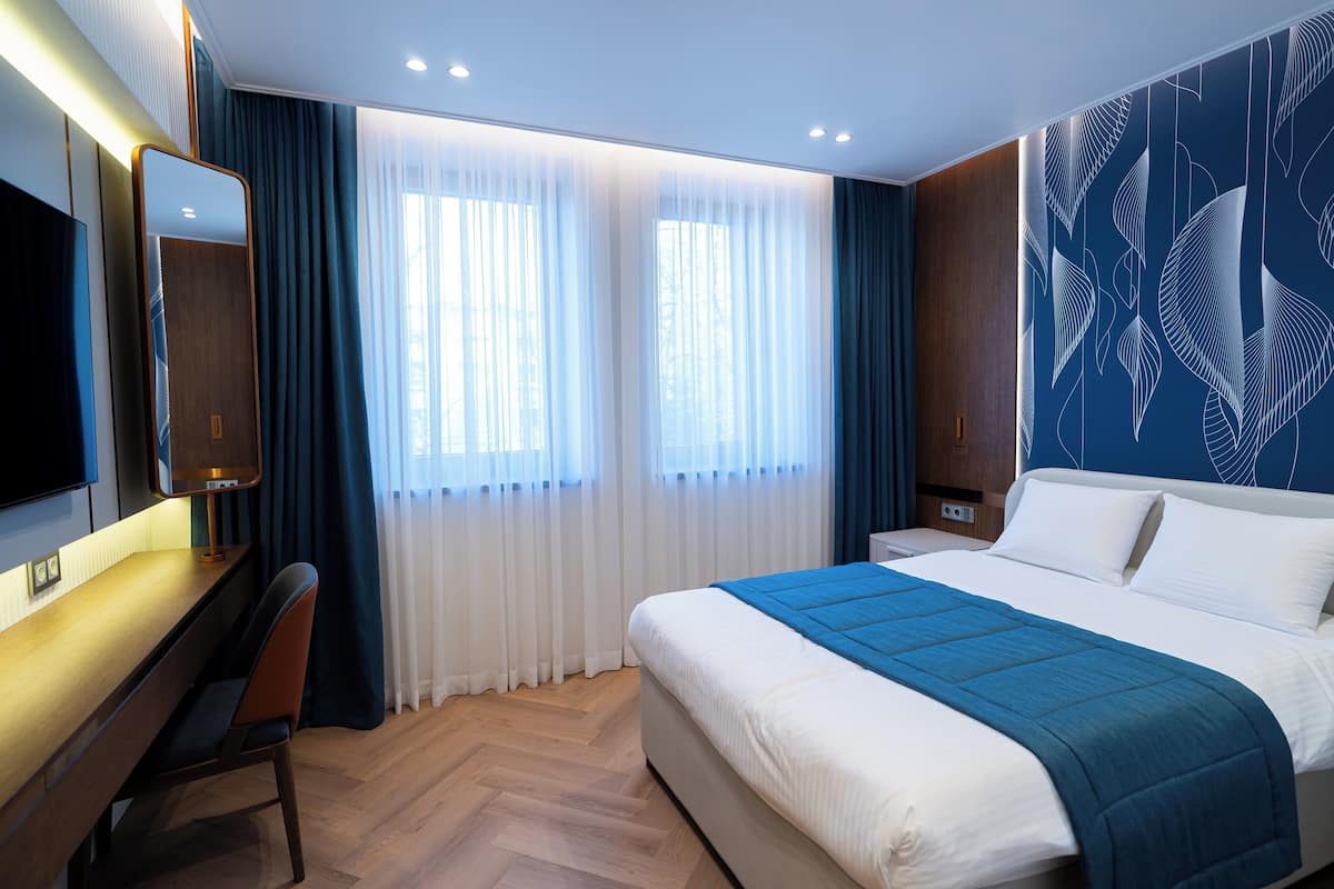 A hotel room with a bed, a desk, a chair, a TV, and a large window with curtains.