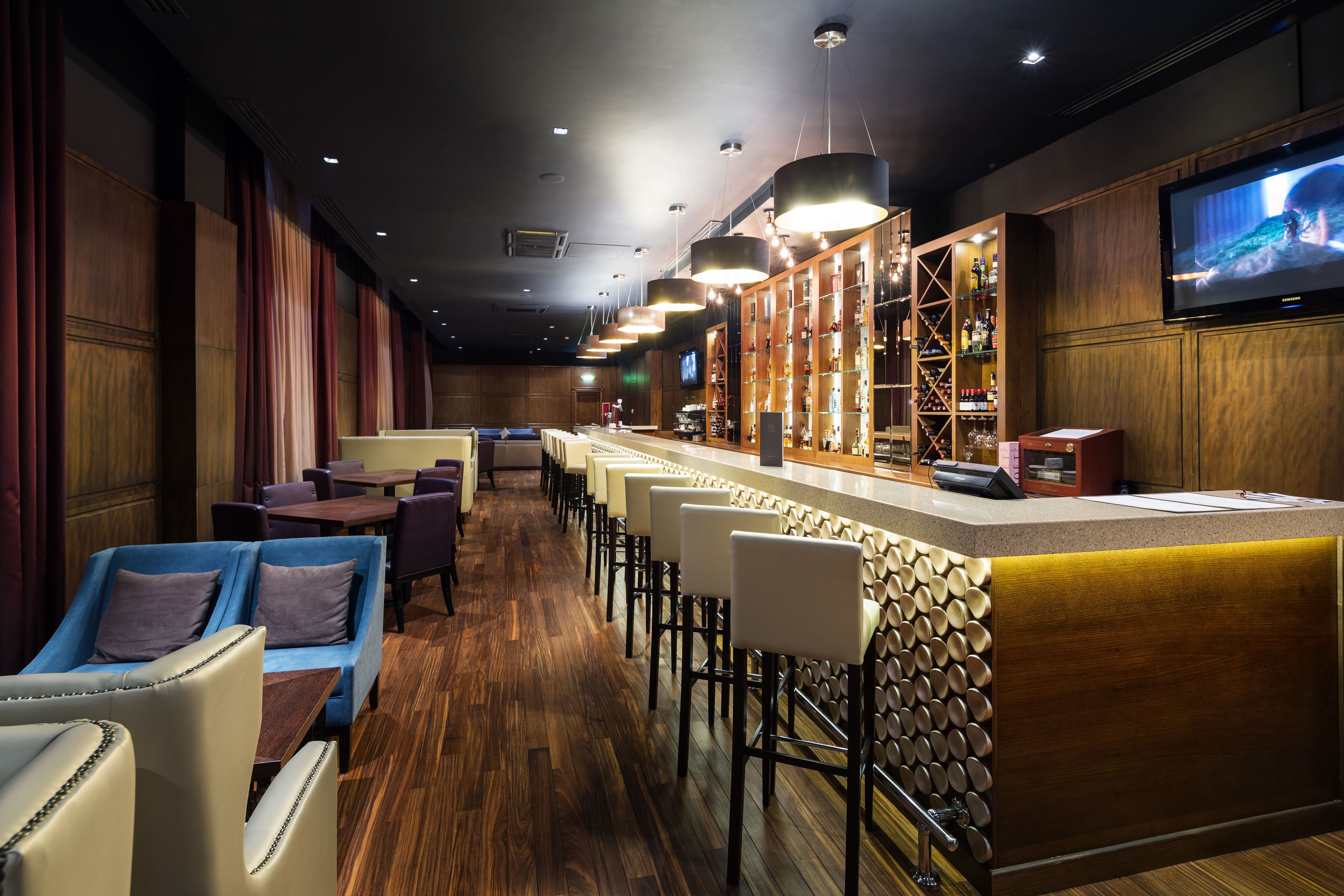 Uma área de bar com painéis de madeira, banquetas e uma tela de televisão.