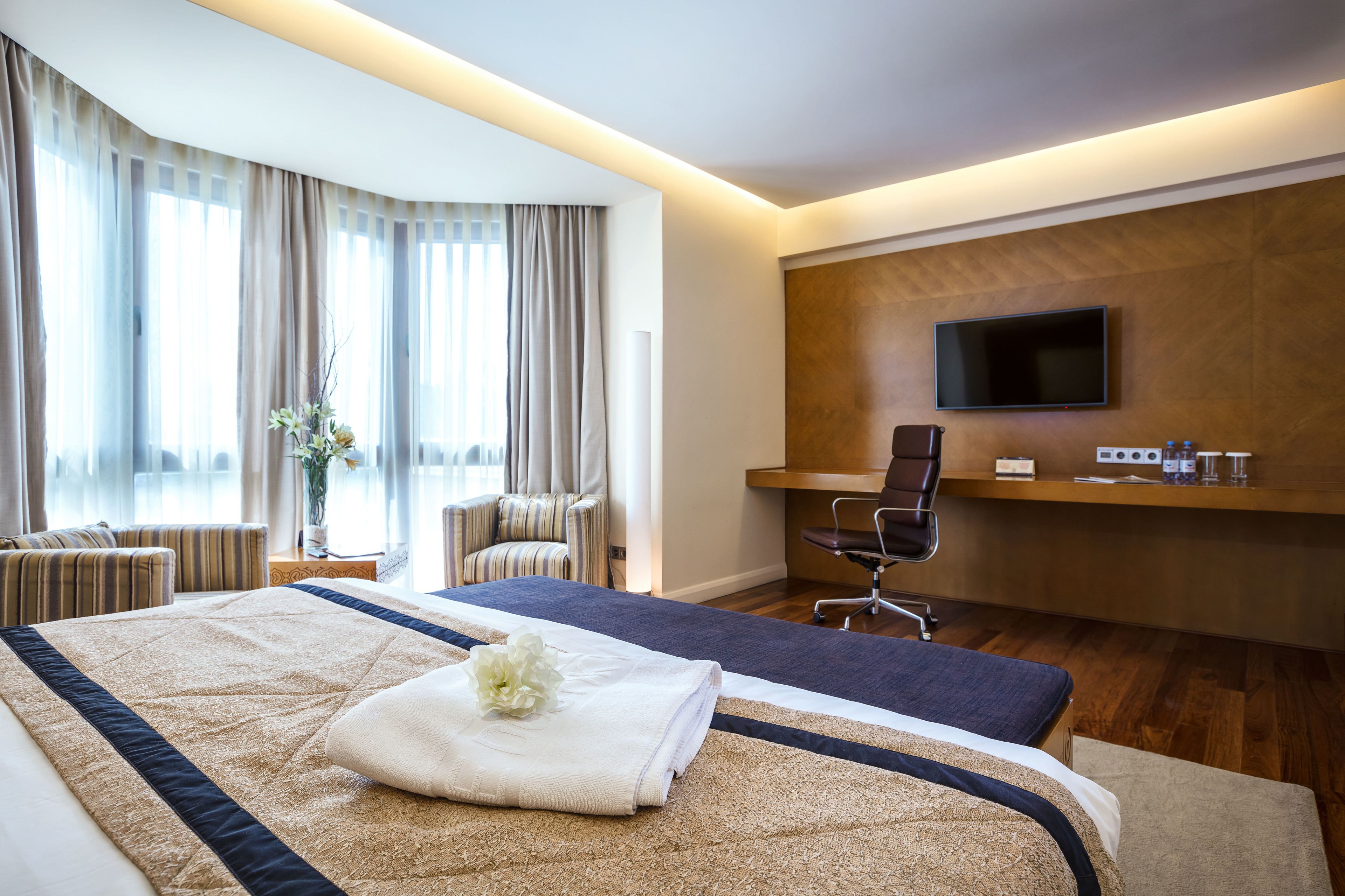 Habitación de hotel con una cama grande, un escritorio con silla, televisor montado en la pared y una ventana con cortinas.