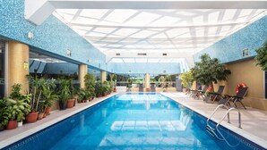 An indoor swimming pool with clear blue water, surrounded by potted plants and sun loungers. - The Dostyk Hotel (Almaty)