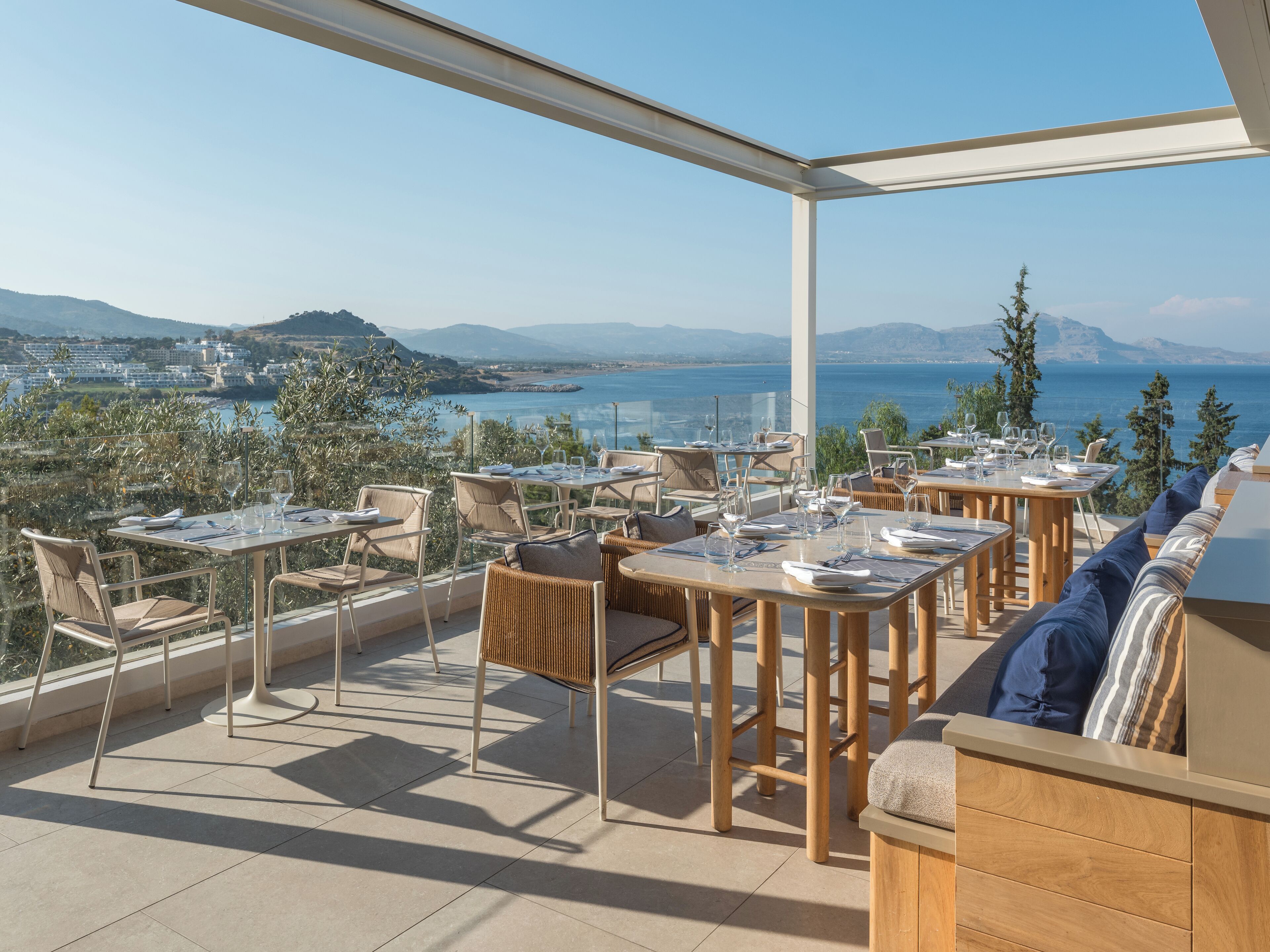A terrace with tables and chairs, overlooking a scenic view of the sea and hills.