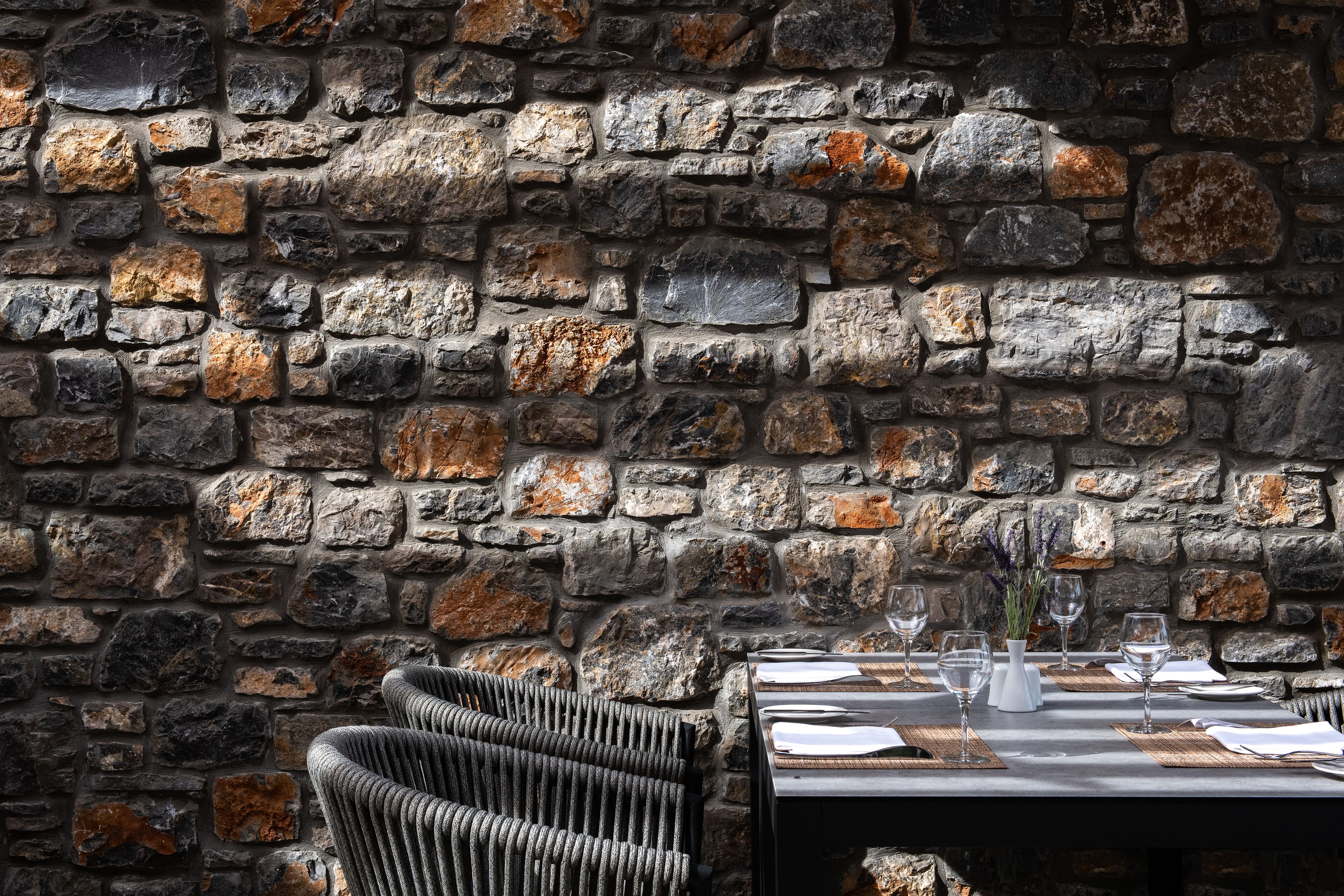 A stone wall restaurant interior with a dining table set for two, including plates, cutlery, and glasses.