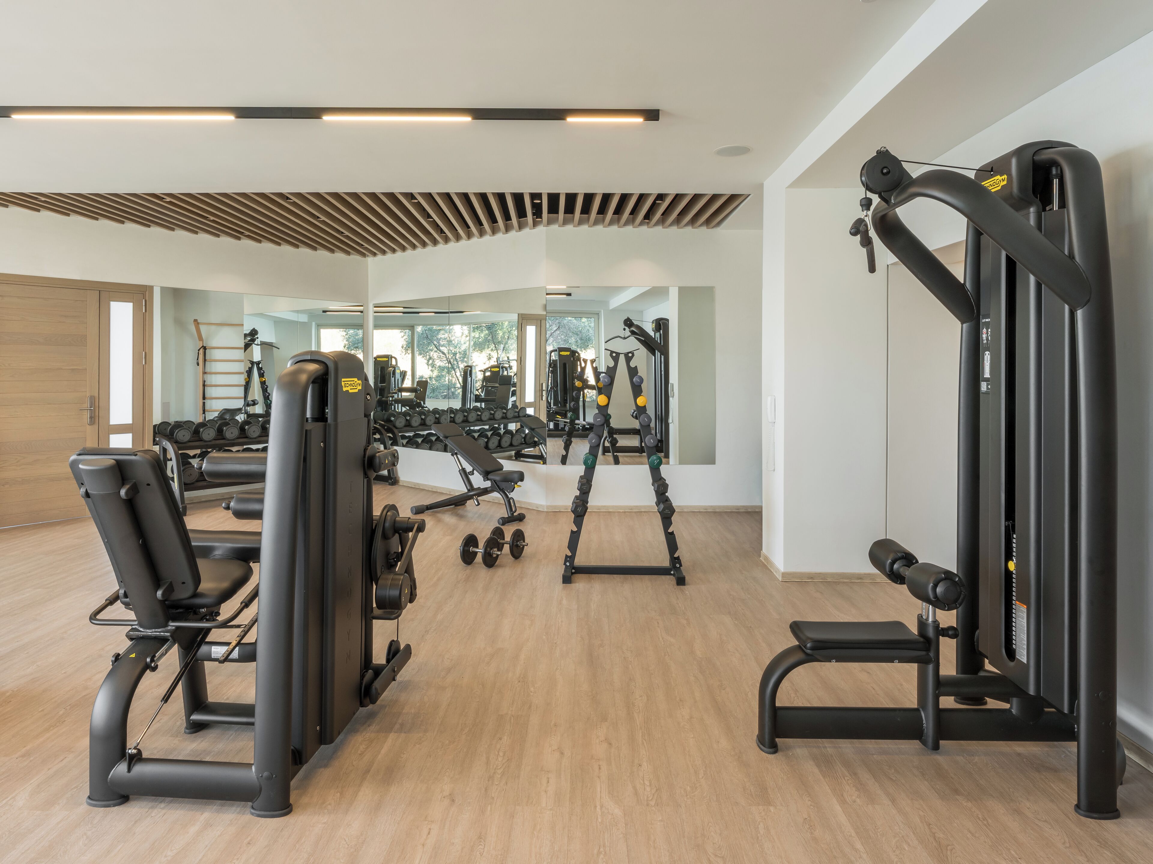Een moderne sportschool met diverse fitnessapparaten, houten vloeren en grote ramen voor natuurlijk licht.