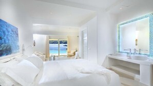 Un dormitorio amplio con una cama grande, un baño con un espejo grande y vistas al mar.
