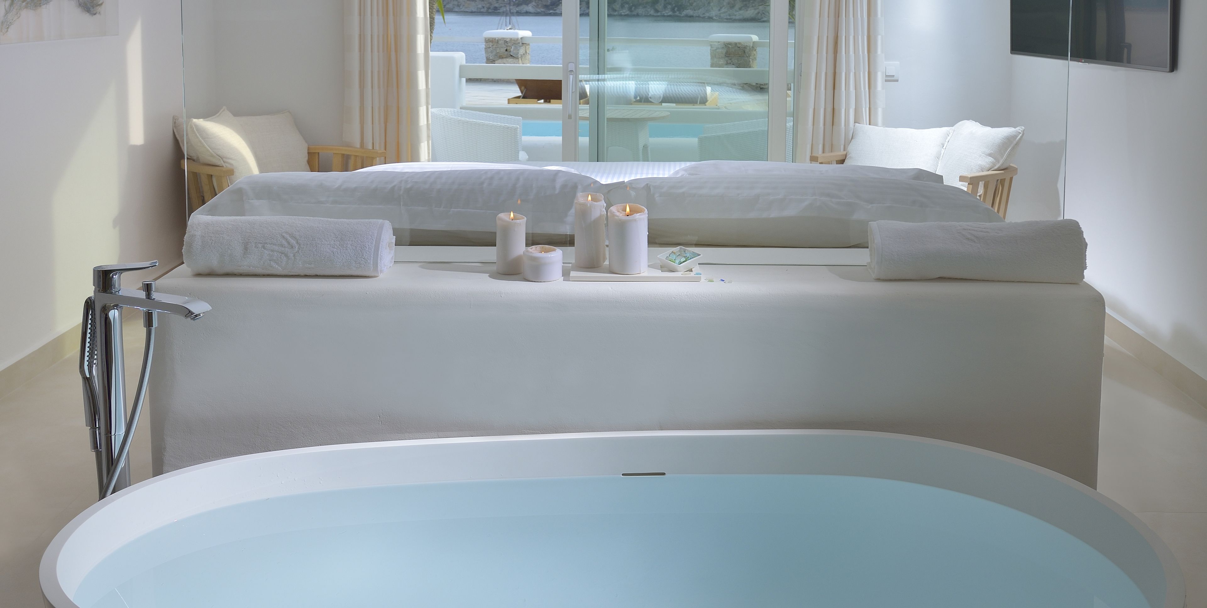 A modern bathroom with a large bathtub, a glass-enclosed seating area with a view of the sea, and a minimalist design.