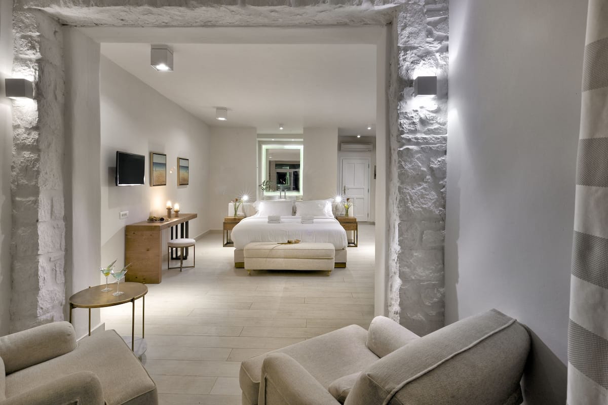 Ein modernes Schlafzimmer mit einem großen Bett, Nachttischen, einer kleinen Sitzecke und Blick ins Bad.