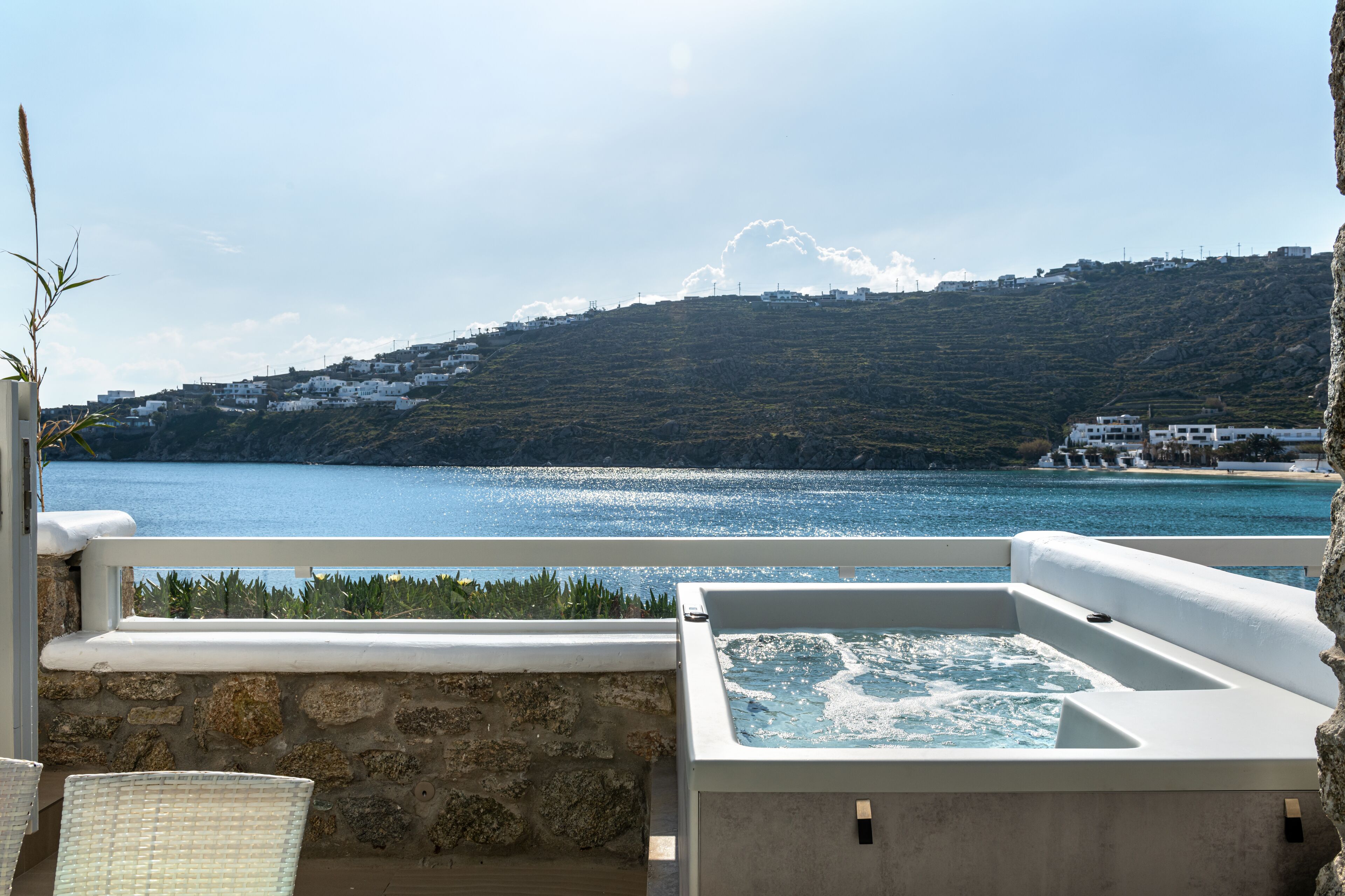 A balcony with a hot tub overlooking a body of water and a hillside with buildings.
