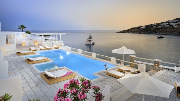 A poolside area with lounge chairs, umbrellas, and a view of the sea. - Nissaki Boutique Hotel (Mykonos)