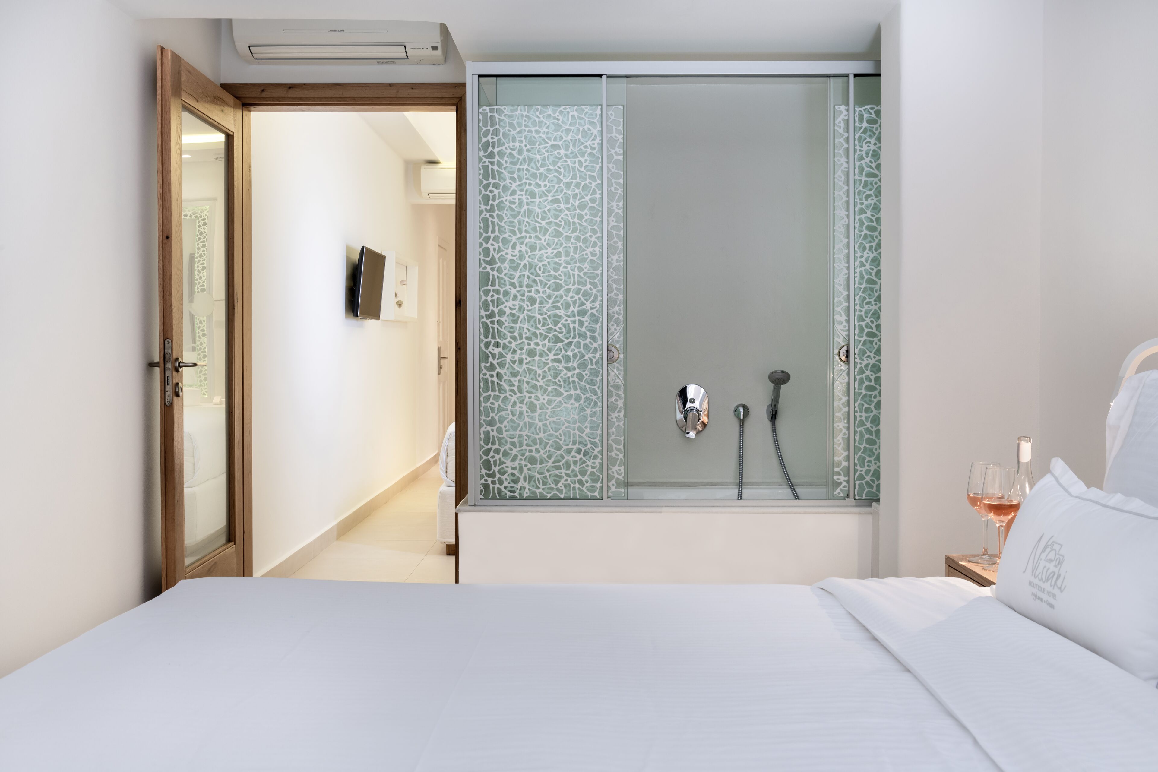Habitación de hotel con cama, cabina de ducha y mesita de noche con una copa de vino.