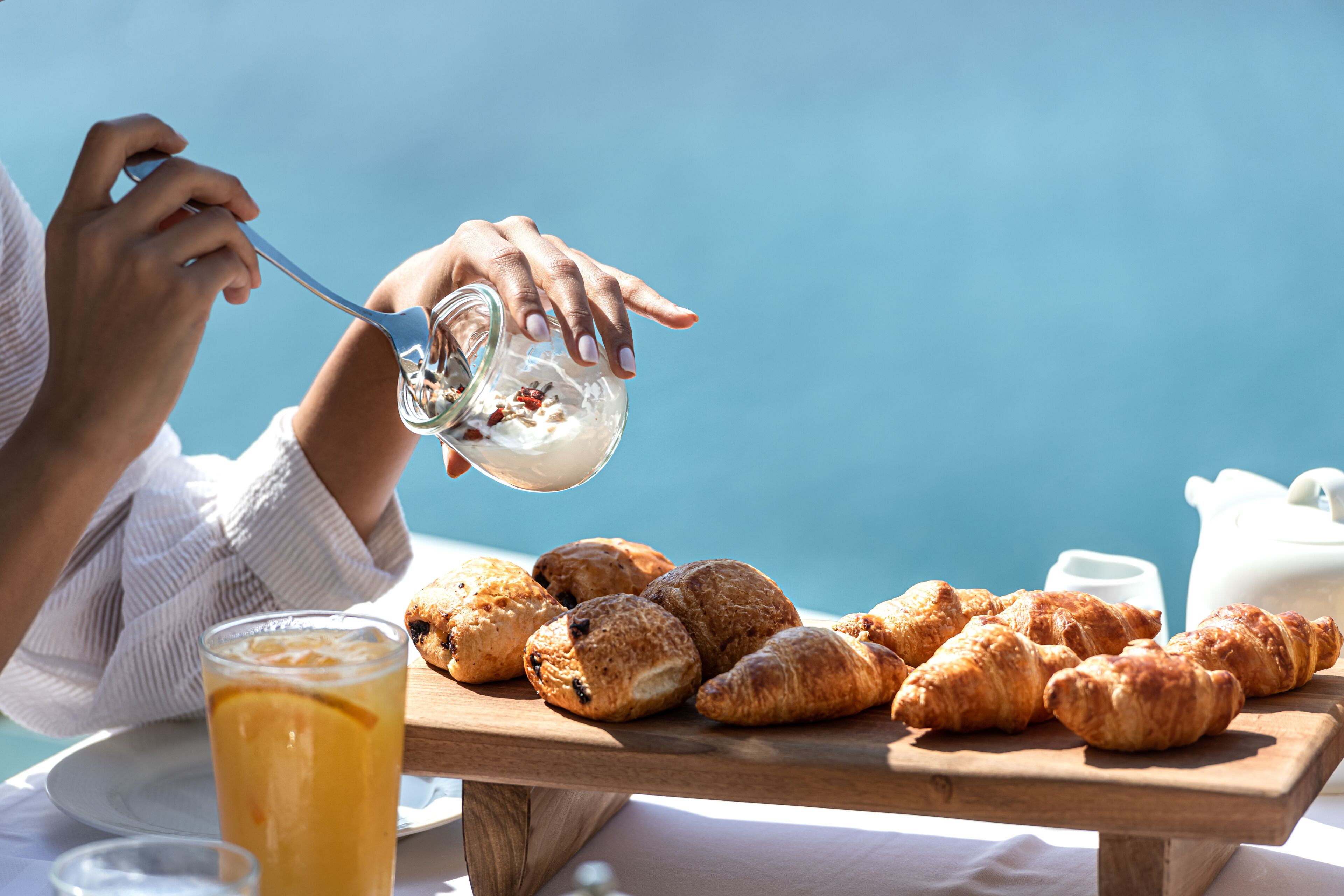 A breakfast setting with croissants and a glass of iced coffee on a wooden board.