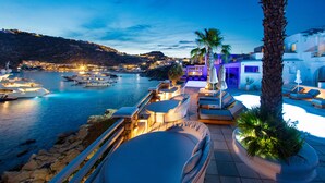 Un resort frente al mar con terraza exterior, piscina y barcos al fondo.