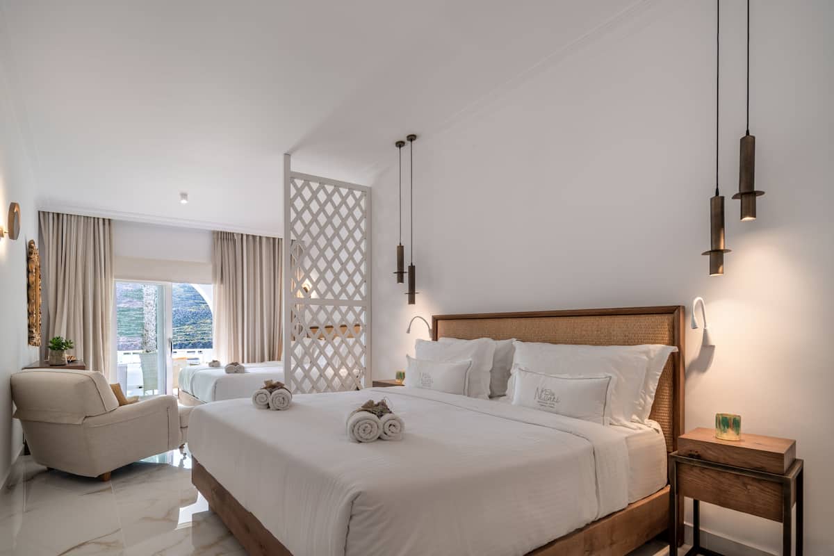 Ein modernes Hotelzimmer mit einem großen Bett, einer Sitzecke mit einem Sessel und einem Balkon mit Vorhängen.