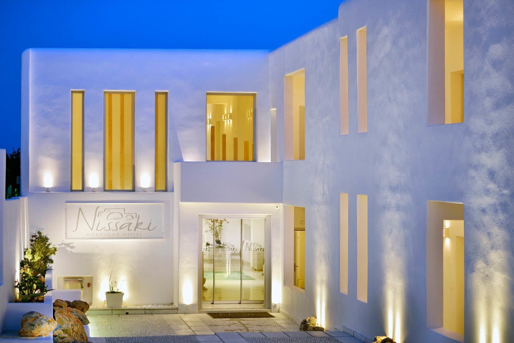 A modern hotel with a minimalist design, featuring a prominent sign for 'Nissaki Boutique Hotel' and a glass entrance.