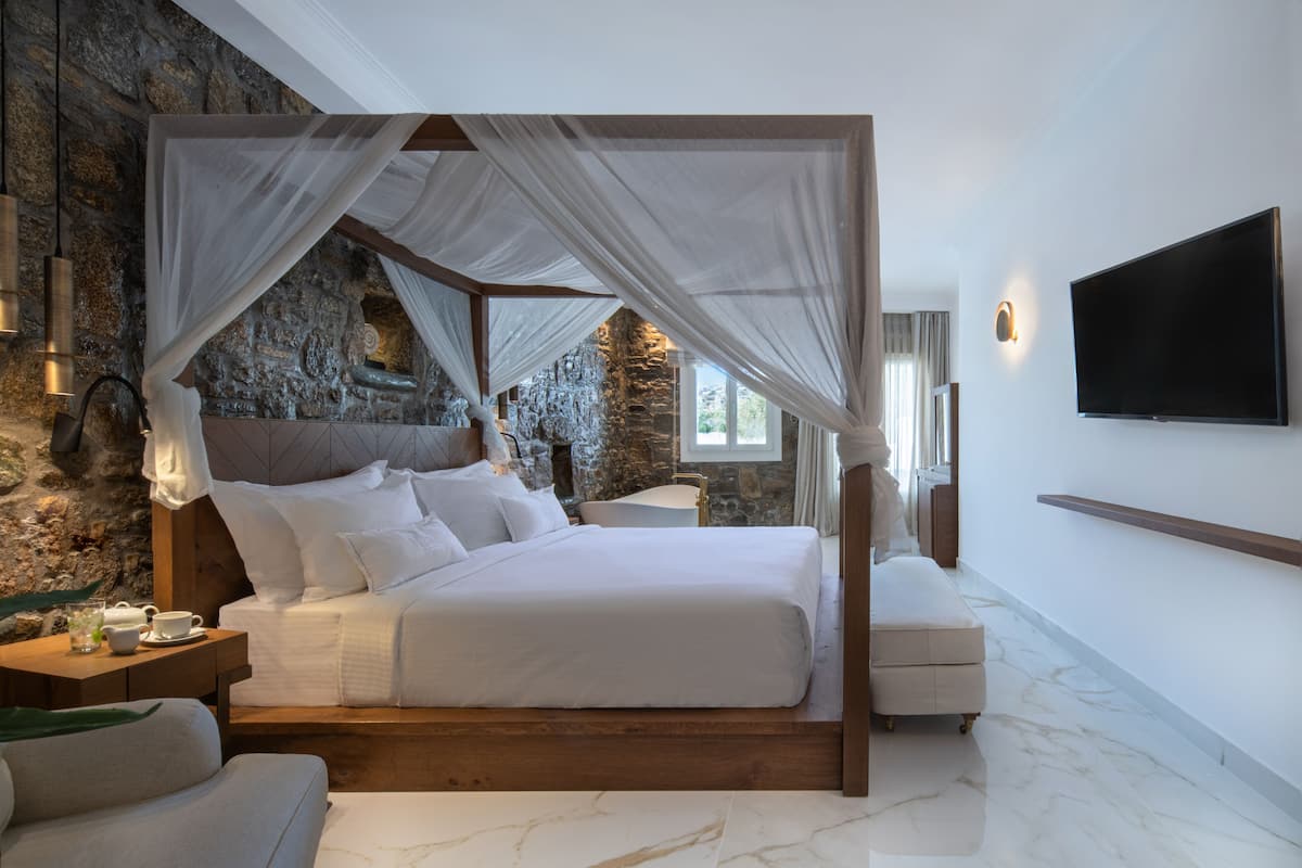 Ein Schlafzimmer mit einer Steinsäule, einem Baldachinbett, einem Flachbildfernseher und einem Marmorboden.
