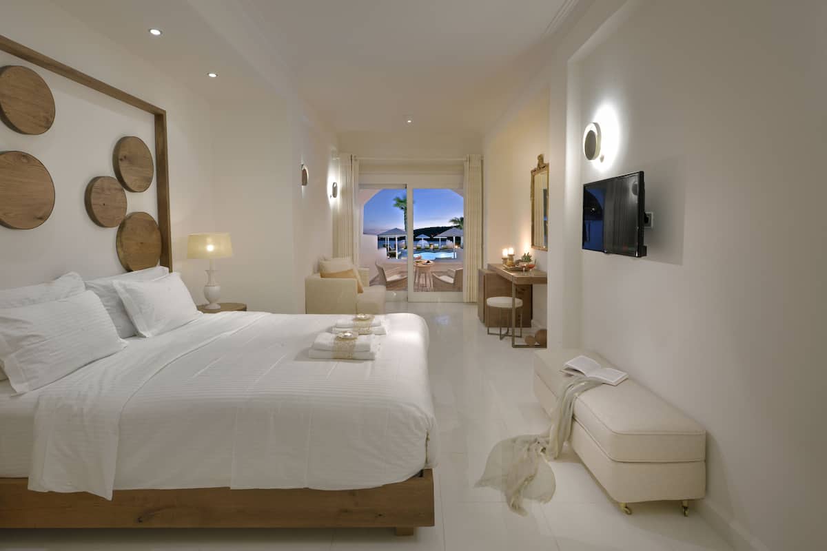 Ein modernes Hotelzimmer mit einem großen Bett, einem Schreibtisch und Blick auf einen Pool und Palmen.