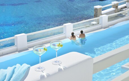 A swimming pool with a clear view of the water, a white poolside area, and two empty glasses on a white surface.