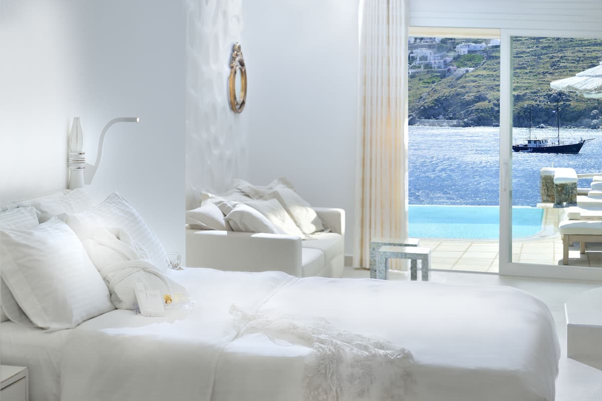 Ein Schlafzimmer mit einem großen Bett, weißen Möbeln und Blick auf das Meer und die Gebäude.