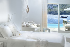 Ein Schlafzimmer mit einem großen Bett, weißen Möbeln und Blick auf das Meer und die Gebäude.