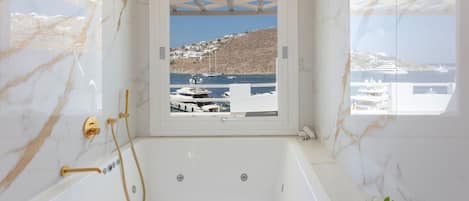 Ένα μπάνιο με μπανιέρα, ντους και θέα σε σκάφη και έναν καταπράσινο λόφο.