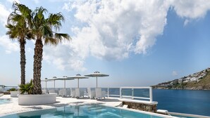 A pool area with lounge chairs, umbrellas, and palm trees. - Nissaki Boutique Hotel (Mykonos)