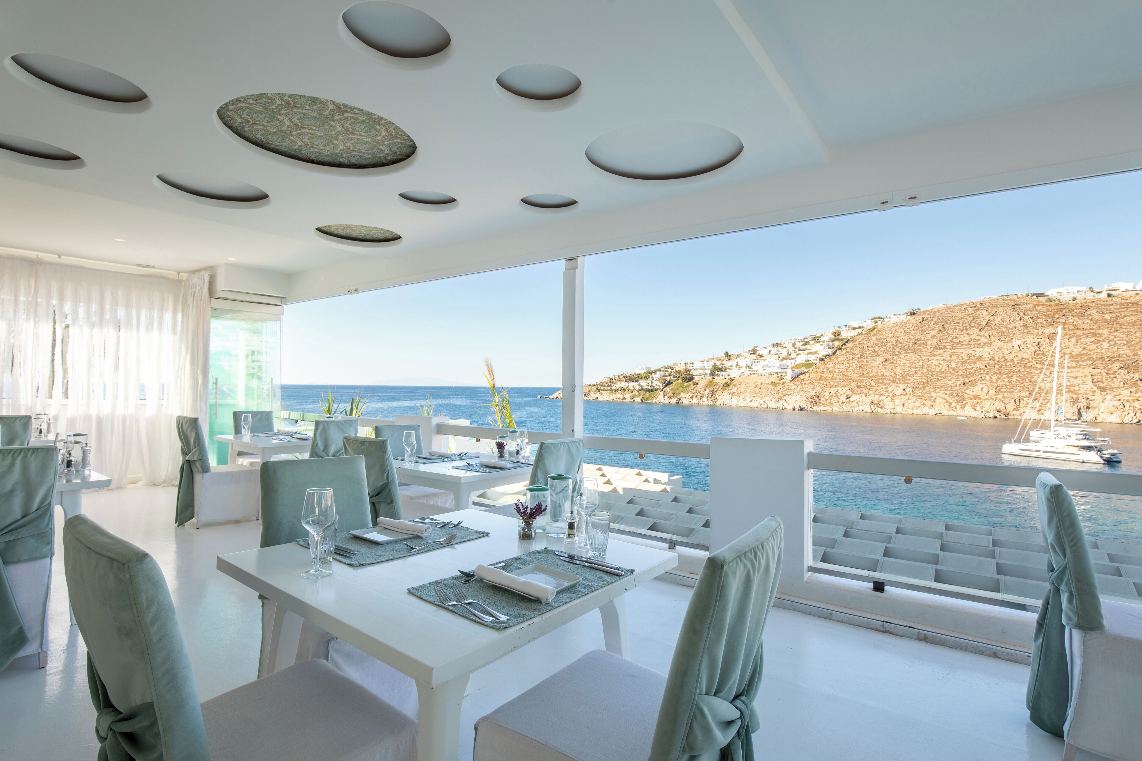 Un comedor moderno con mobiliario blanco y vista al mar.