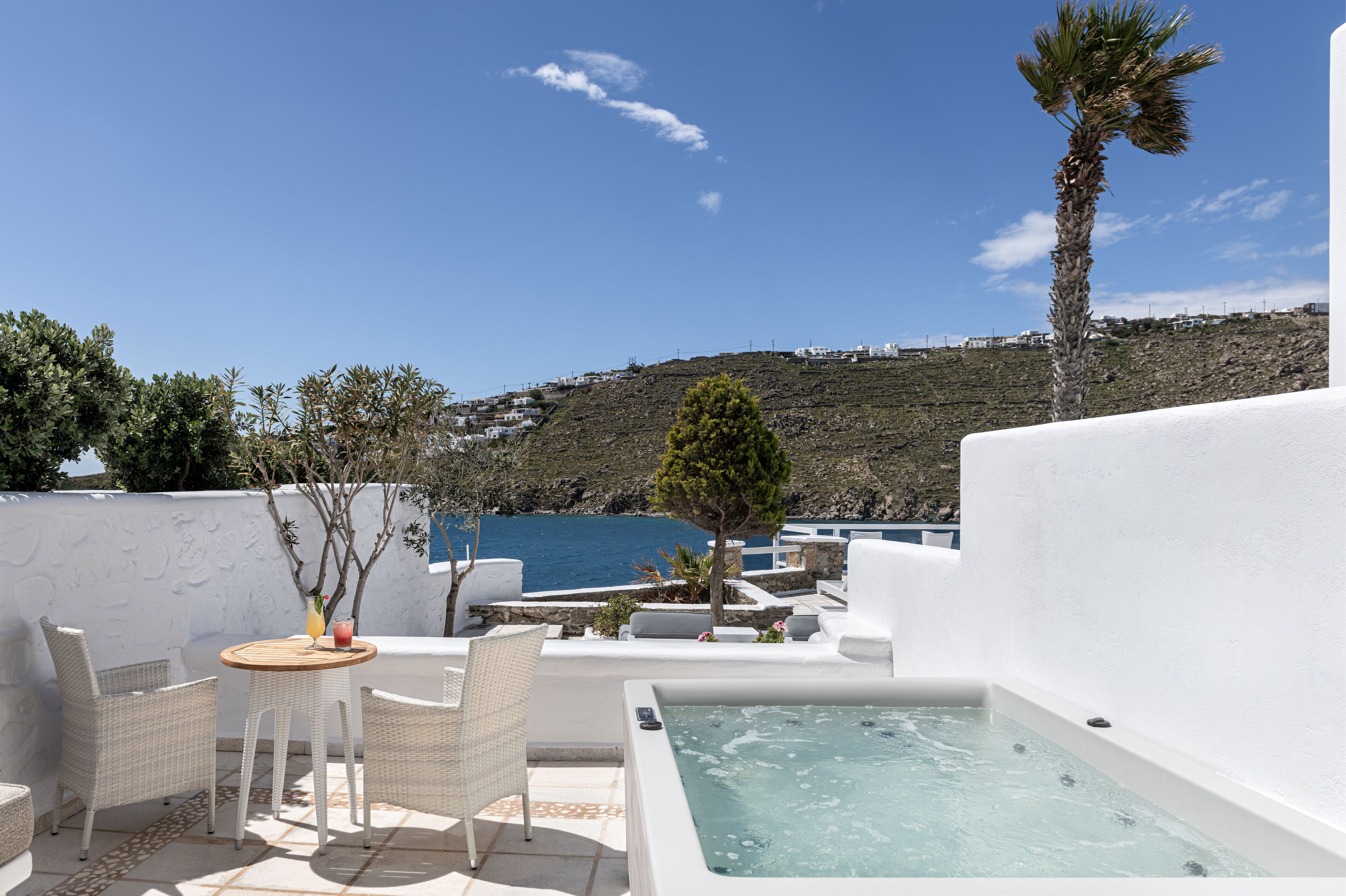 Una terraza en la azotea con jacuzzi, muebles de mimbre y vistas al mar y las colinas.