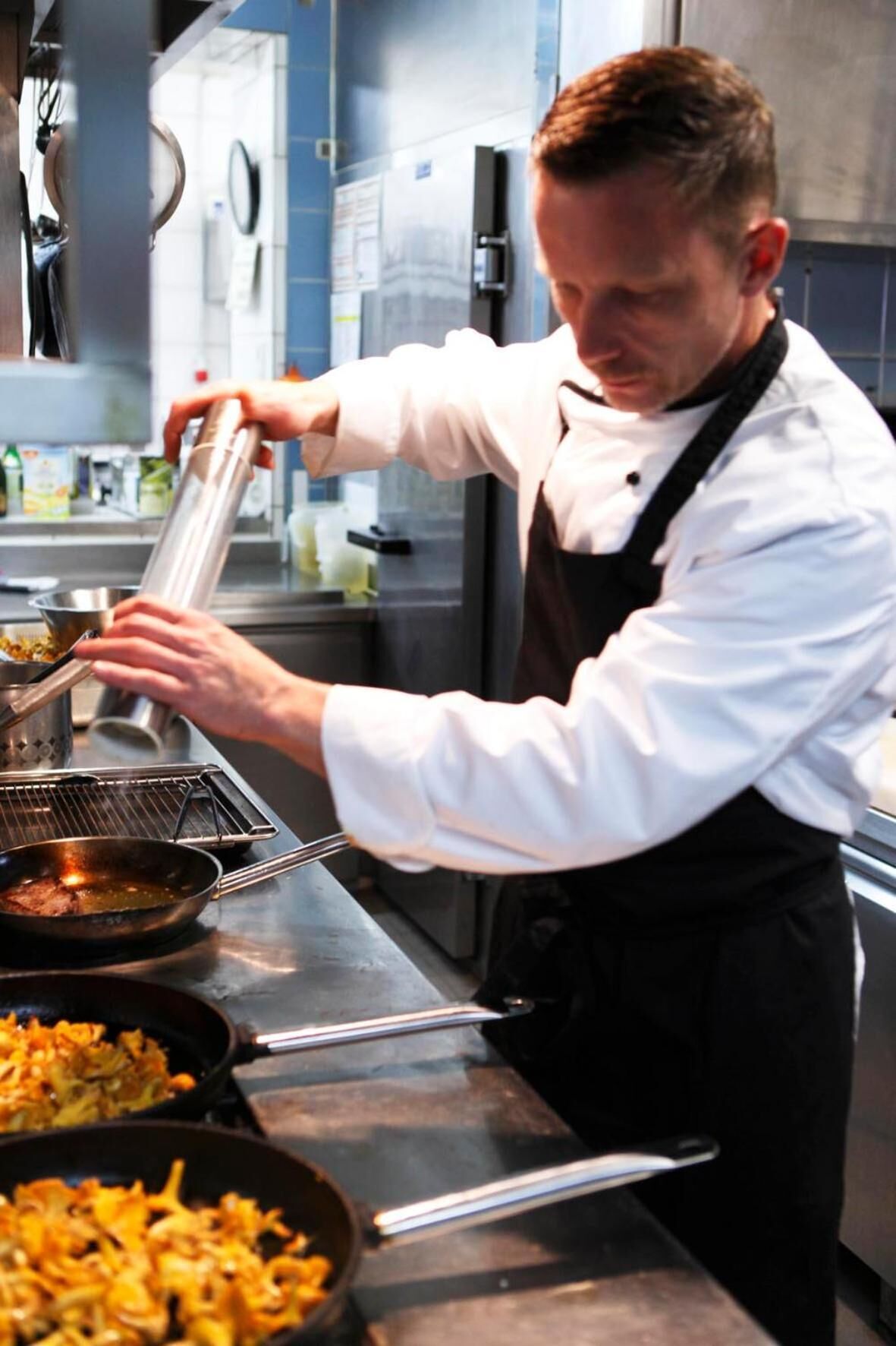 A chef preparing food in a commercial kitchen with stainless steel surfaces and various cooking utensils.