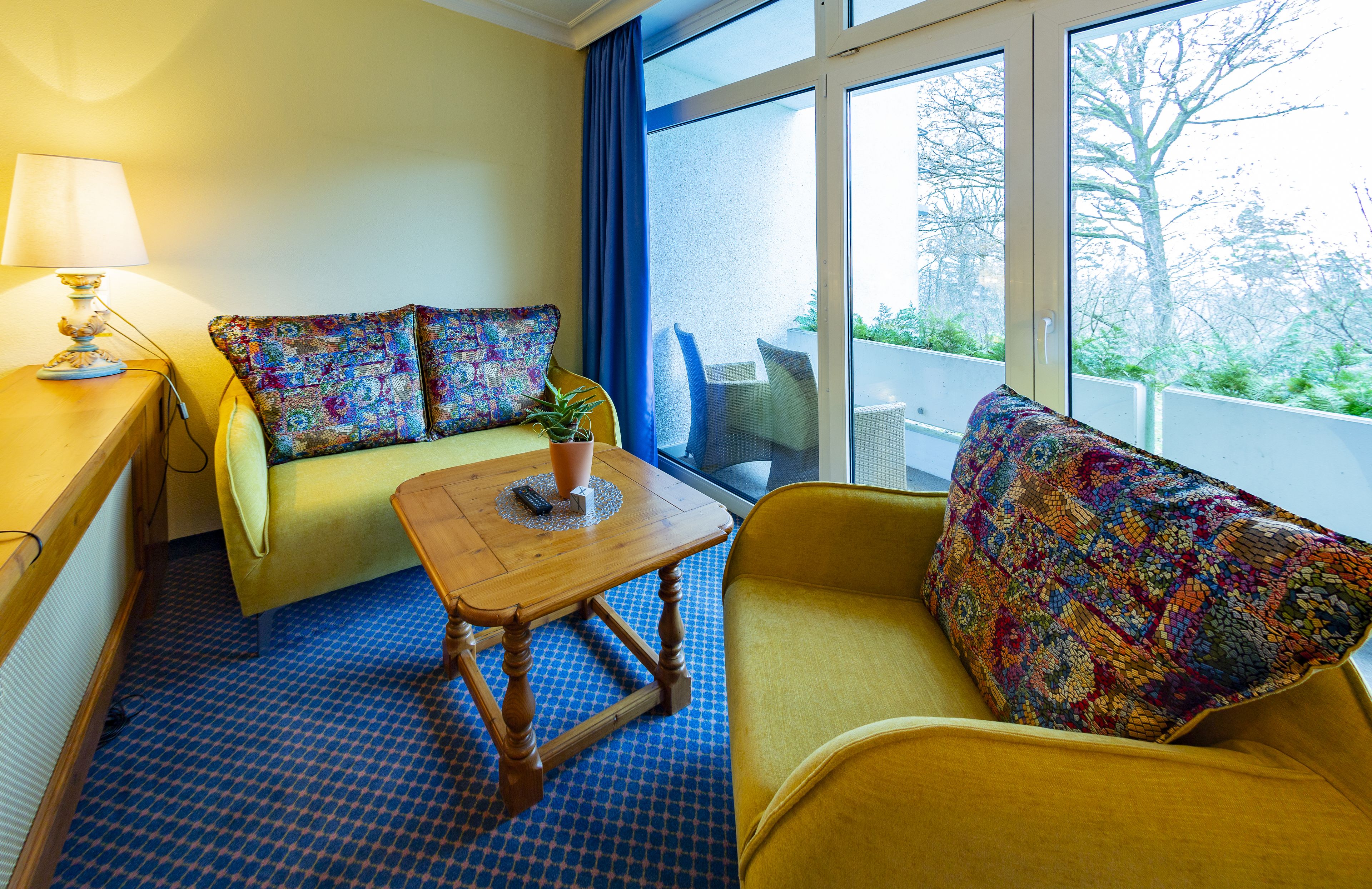 A room with a sofa, armchair, and a small table with a lamp.