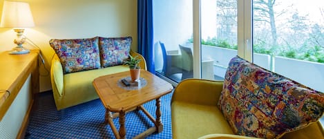 A room with a sofa, armchair, and a small table with a lamp.