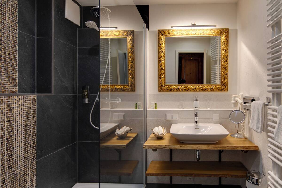 Ein modernes Badezimmer mit einer gläsernen Duschkabine, einem Waschtisch mit weißem Waschbecken und einem goldfarben gerahmten Spiegel.