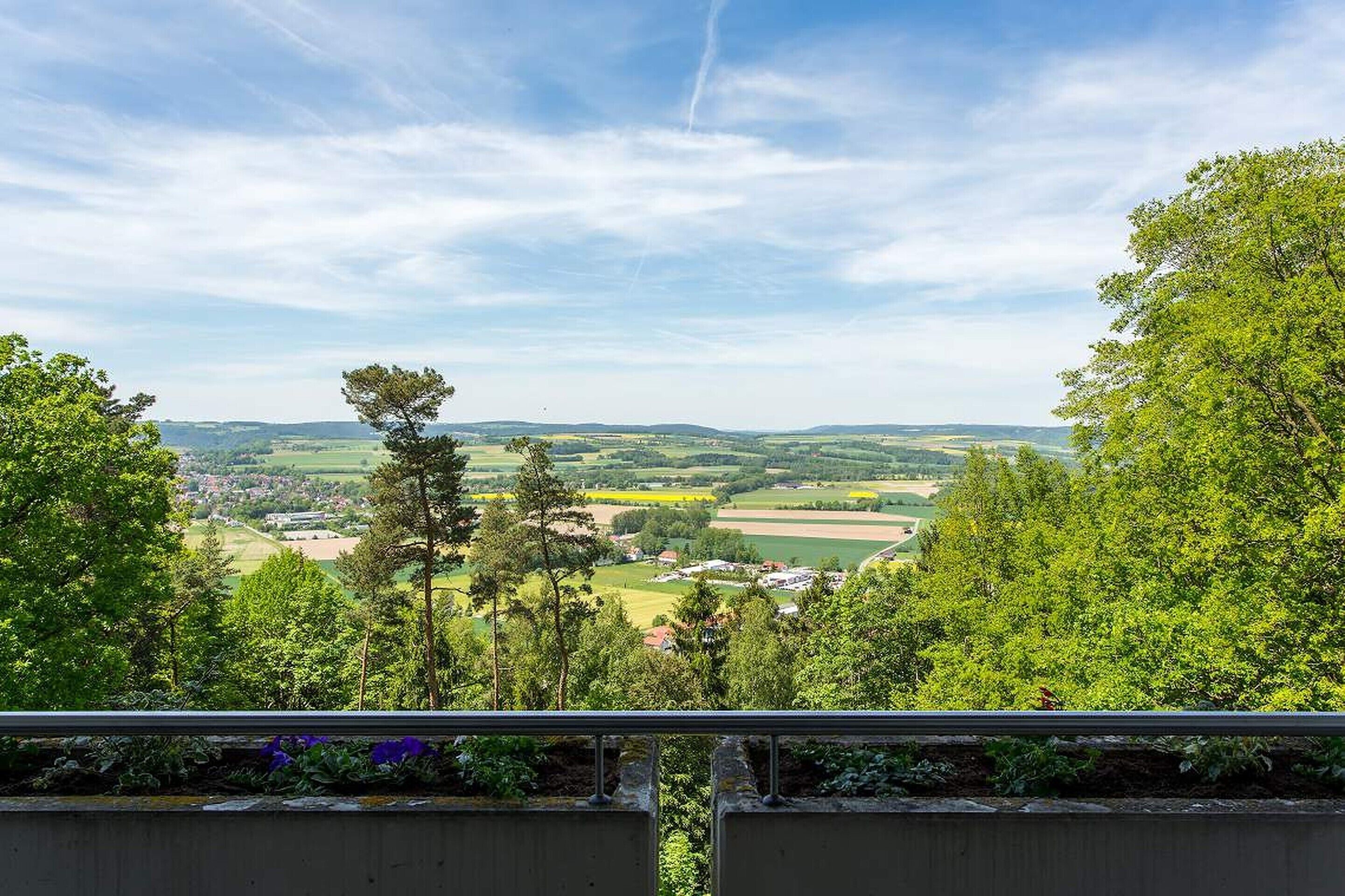 A scenic view from a balcony overlooking a rural landscape with fields and scattered buildings.