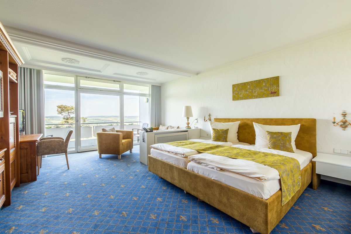 Ein Hotelzimmer mit einem großen Bett, einem Schreibtisch, einem Stuhl und Blick ins Freie.
