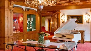 A grand room with a chandelier, a grand piano, and ornate wooden paneling. - Hotel Reiterhof Bellevue Spa & Resort (Wirsberg)