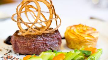 Bife coberto com anéis de cebola, acompanhado de um pastel e decorado com cebolinha e cenouras.