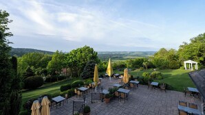 An outdoor patio with tables and chairs, surrounded by greenery and a view of the countryside. - Hotel Reiterhof Bellevue Spa & Resort (Wirsberg)