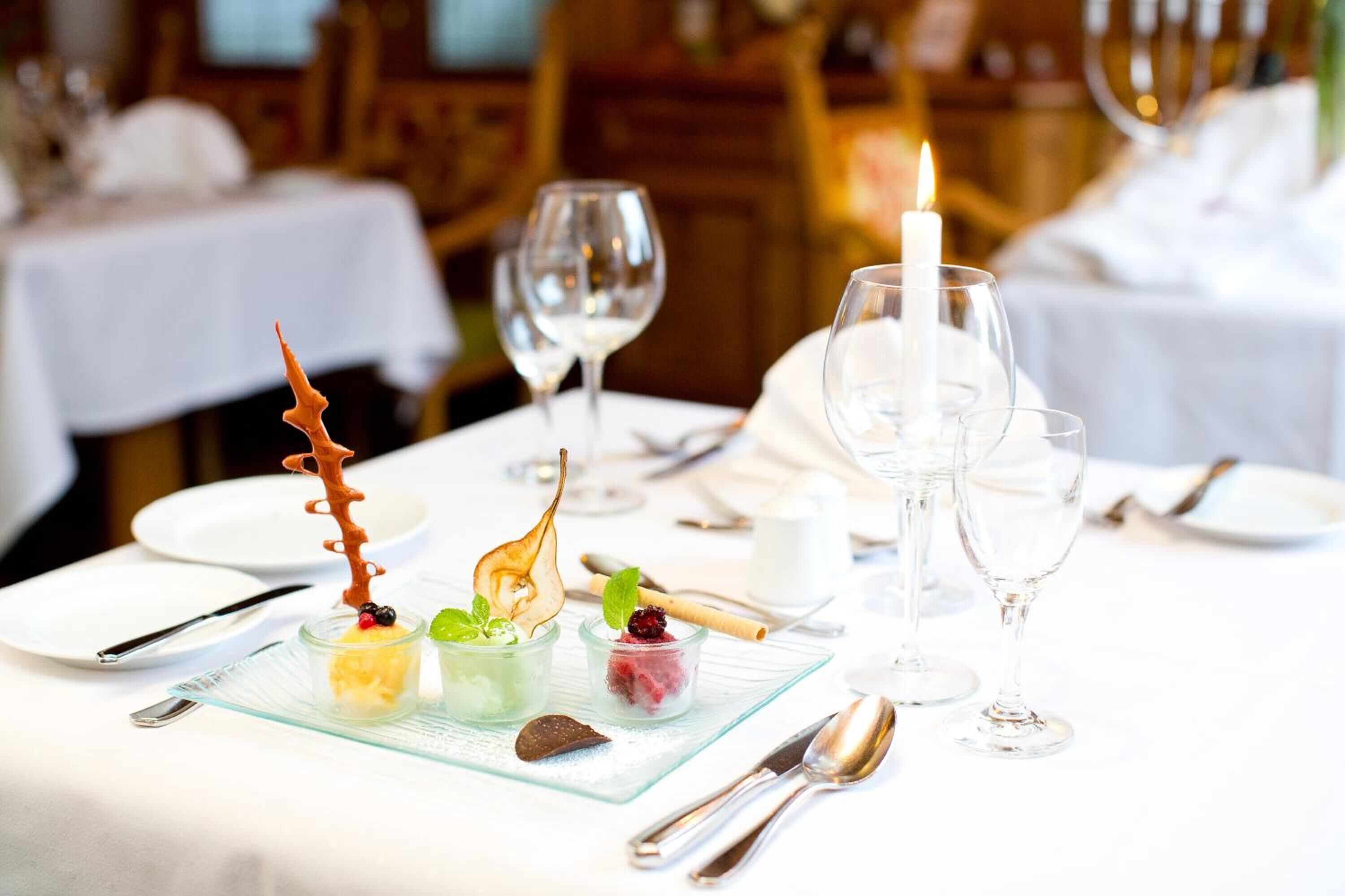 Une table à manger avec trois verres à dessert, une bougie et des couverts.