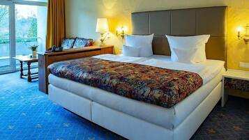 Habitación de hotel con una cama grande, una mesita de noche, una lámpara y vistas al exterior.