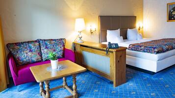 Habitación de hotel con sofá, una pequeña mesa con una planta, cama con colcha colorida y teléfono fijo en la pared.