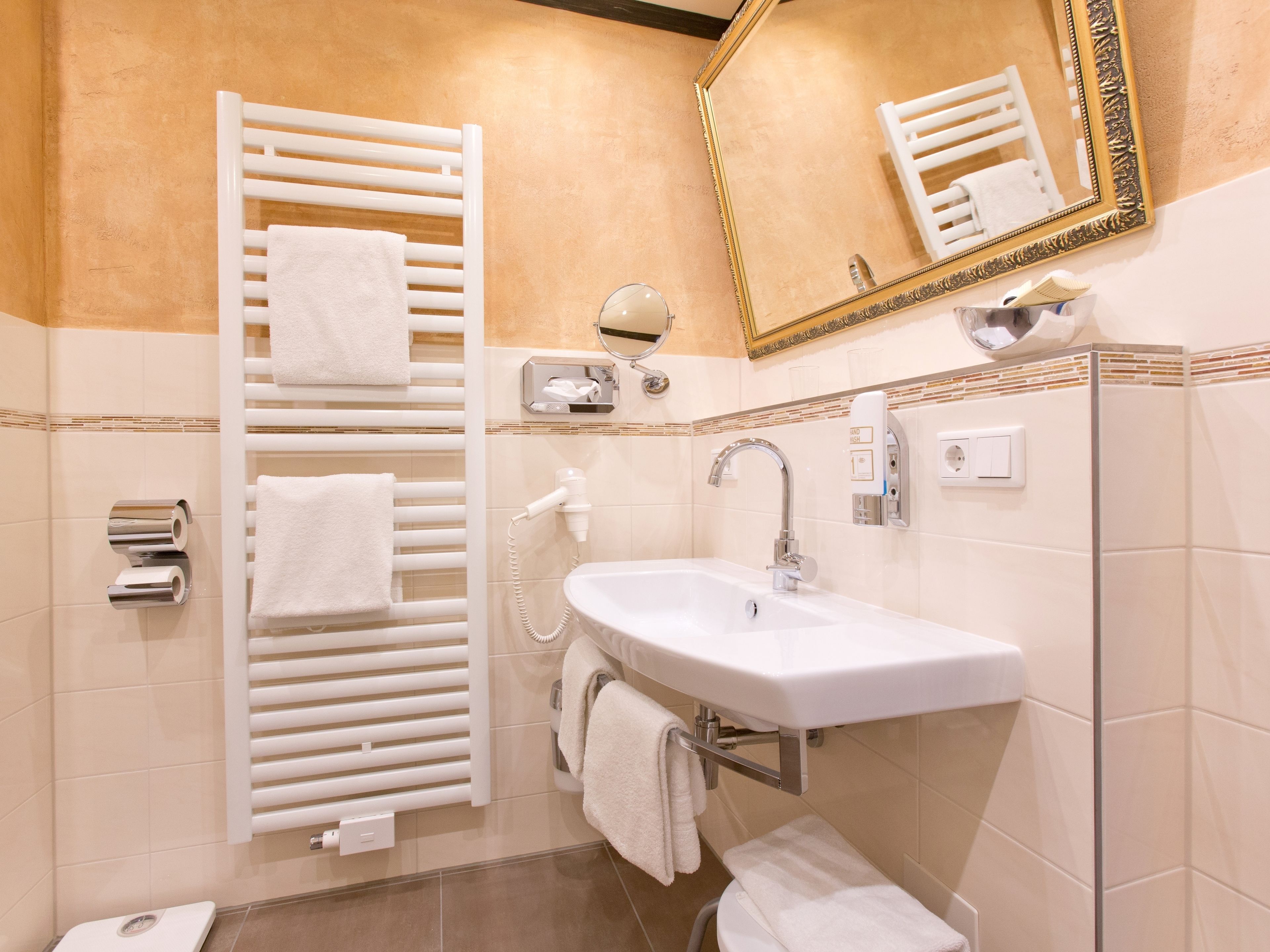A modern bathroom with a white sink, towel rack, and a mirror with a gold frame.