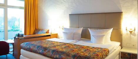 Une chambre d’hôtel avec un grand lit, une tête de lit en bois, une table de chevet et une fenêtre avec des rideaux.