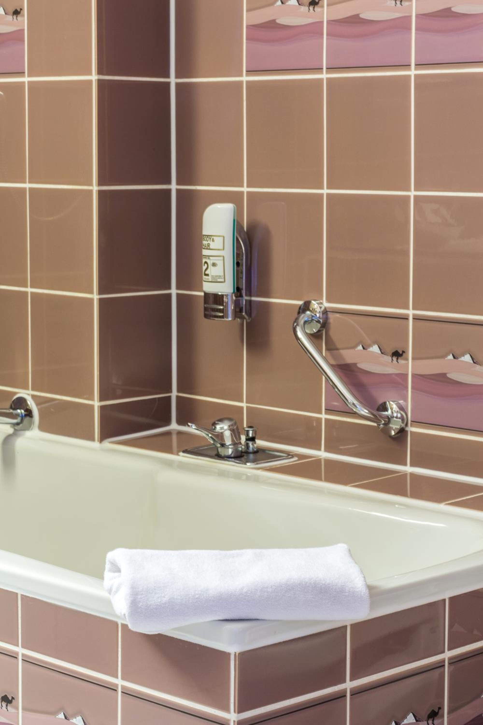 Ein Badezimmer mit einer Badewanne, einem Handdesinfektionsspender und einer Handstange.