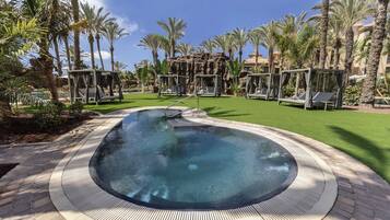 A hot tub surrounded by palm trees and a brick walkway.