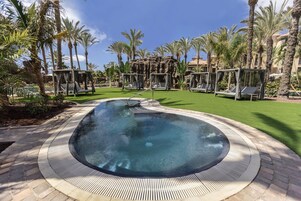 A hot tub surrounded by palm trees and a brick walkway.