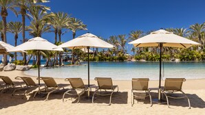 A beachside pool area with lounge chairs and umbrellas, surrounded by palm trees and a clear blue sky. - Lopesan Costa Meloneras Resort & Spa   (San Bartolomé de Tirajana)