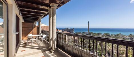A balcony with a view of the sea, a lighthouse, and a cityscape.