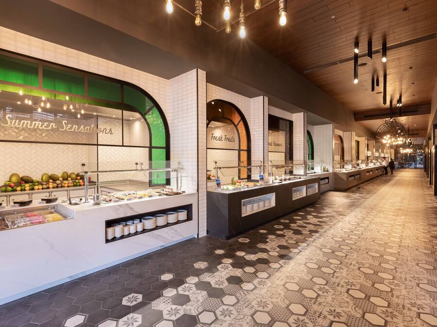 A long, well-lit corridor with hexagonal patterned flooring and multiple food display counters labeled "Summer Sensations" and "Fresh Fruits".