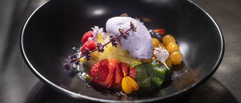 A dessert with various fruits and a scoop of ice cream on a black plate.
