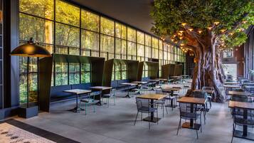 A spacious indoor area with multiple tables and chairs, large windows with a view of trees, and a large artificial tree with lights.